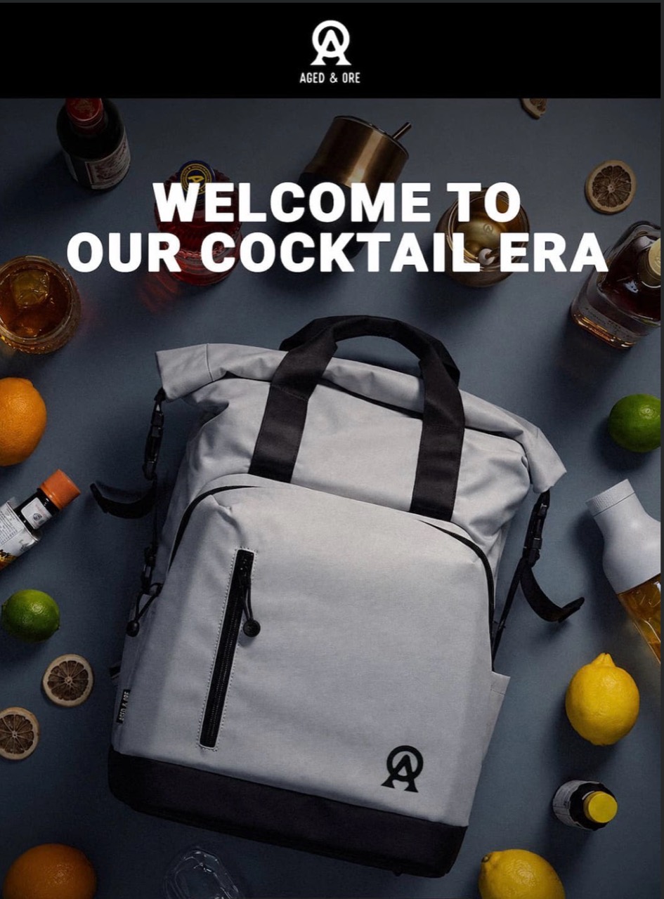 Aged & Ore promotional artwork showing the grey Oasis Bag surrounded by cocktail glasses, bottles and citrus
