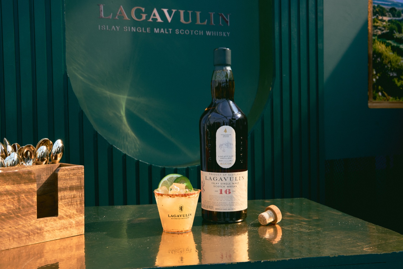 Lagavulin 16 bottle beside a cocktail on a green bar