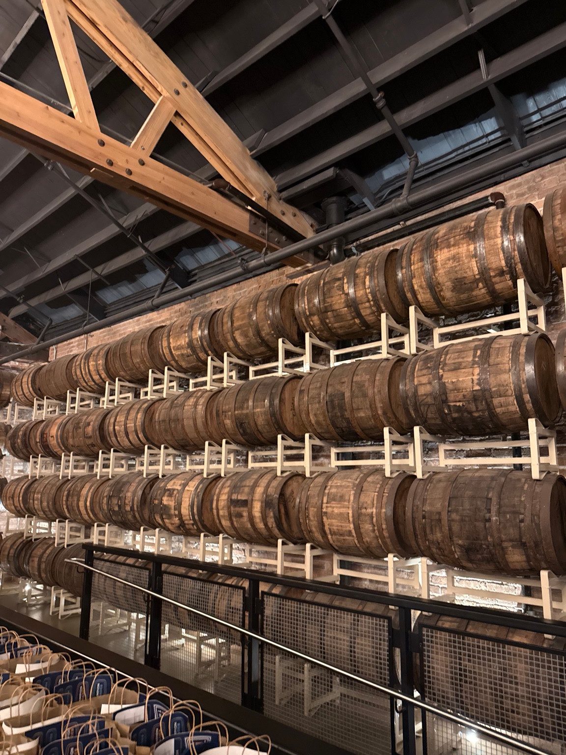 Wide view of stacked wooden barrels along a brick wall beneath exposed beams at Goose Island Barrel House in Chicago.