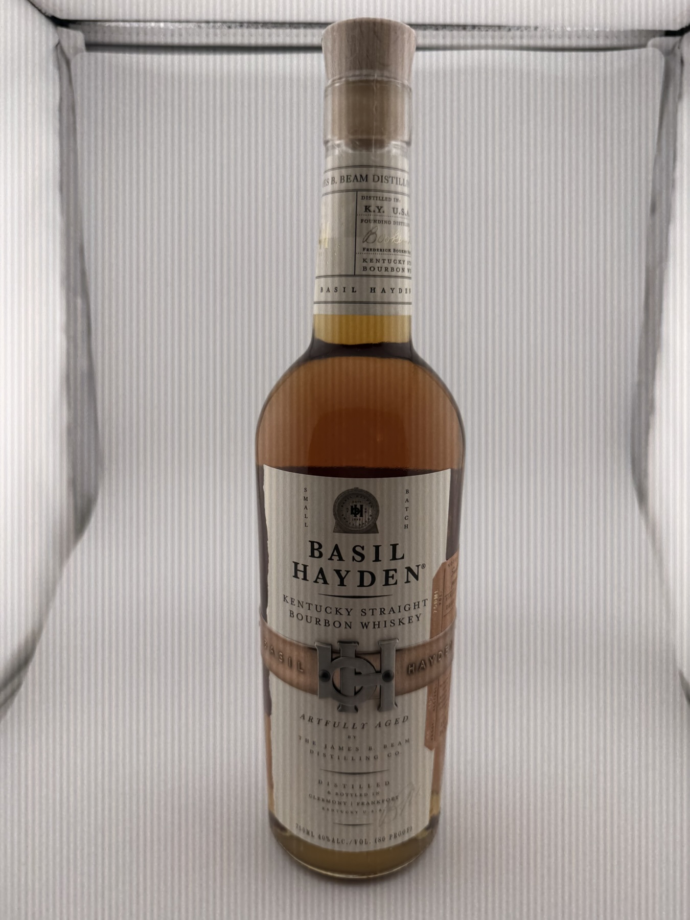 Front of a Basil Hayden bottle with a cream paper label, copper-coloured band and BH monogram