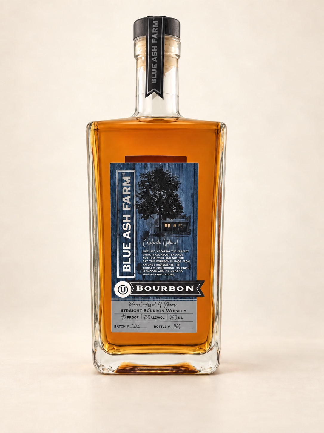 Blue Ash Farm Straight Bourbon bottle with amber whiskey, a dark blue tree-and-cabin label and a black ribbon